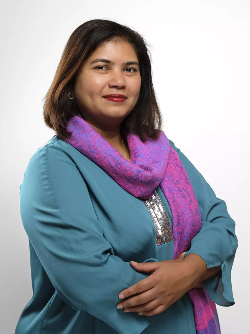 Woman in teal jacket and pink scarf, facing camera with confident expression.